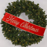Ribbon banner in red with gold gilded Merry Christmas lettering, draped across a pine wreath.