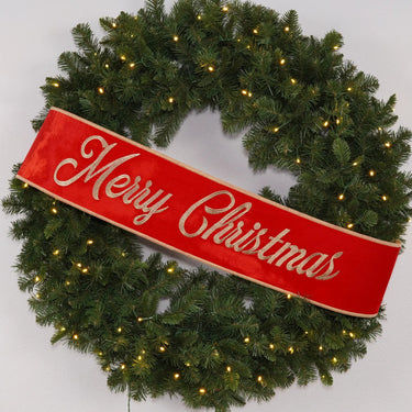 Ribbon banner in red with gold gilded Merry Christmas lettering, draped across a pine wreath.