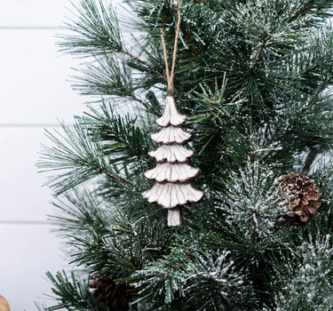 Resin brown-cream tree ornament by Melrose hanging on a jute string amid snow-dusted pine needles
