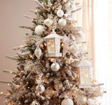 Lit Snowy Wood Snowflake Lantern by Melrose on a snow-dusted Christmas tree with ornaments
